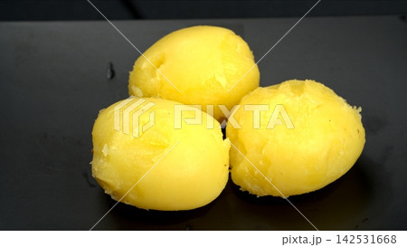 Three peeled boiled yellow potatoes resting on sleek black plate, nutritious organic root vegetable culinary ingredient Three peeled boiled yellow potatoes resting on sleek black plate, nutritious organic root vegetable culinary ingredient 142531668