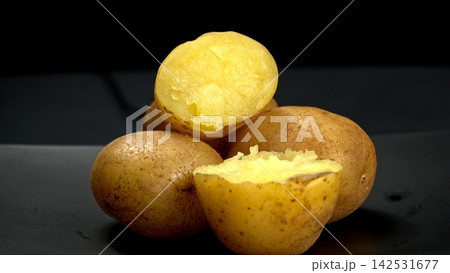 Closeup of warm boiled potatoes with skins on and halved revealing fluffy steamy yellow flesh, rustic organic root meal 142531677