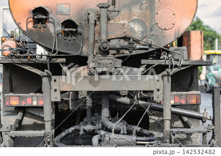 A truck equipped for asphalt application is parked on a road. The back of the truck shows pipes and machinery used for the work A truck equipped for asphalt application is parked on a road. The back of the truck shows pipes and machinery used for the work 142532482