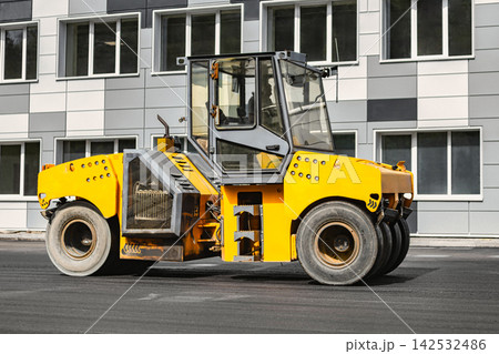 A heavy-duty roller compacts asphalt at a construction site. Road reconstruction. Heavy equipment rental 142532486