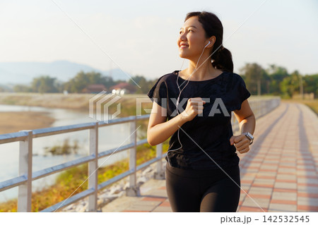 Asian woman jogging on pathway during sunny morning outdoors Asian woman jogging on pathway during sunny morning outdoors 142532545