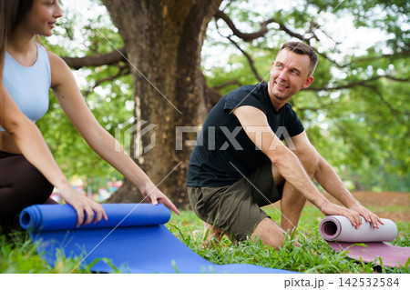 Couple unrolling yoga mats on grass under trees for workout 142532584