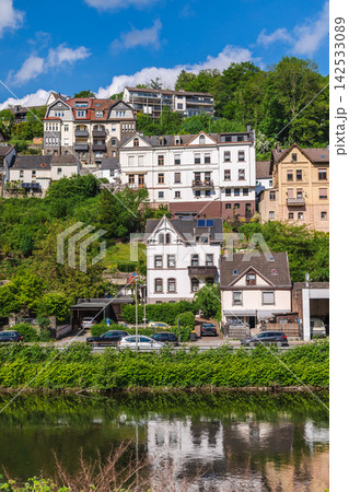 Riverside Houses on Lush Hillside Under Blue Sky Riverside Houses on Lush Hillside Under Blue Sky 142533089