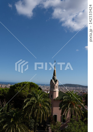 Ornate church tower rises above palm trees with colorful ceramic tiles and decorative facade details. Blue sky, coastal city buildings, hills, and sea create distinctive architectural landmark view. 142533424