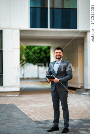 Confident businessman holding tablet standing in city corporate environment 142533585