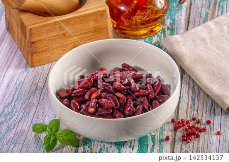 Red kidney beans in a white bowl on a rustic wooden table with fresh basil and red peppercorns Red kidney beans in a white bowl on a rustic wooden table with fresh basil and red peppercorns 142534137