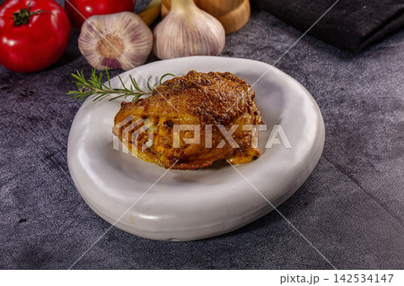 Roasted chicken thigh with rosemary garnish on a white plate with fresh tomatoes and garlic 142534147