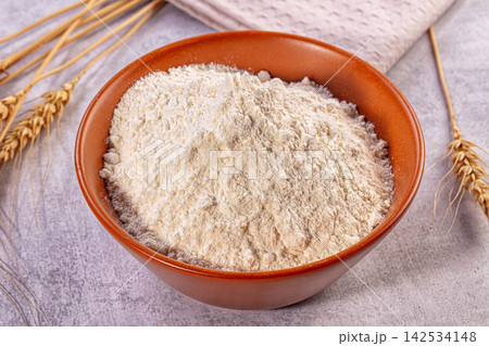 White flour in terracotta bowl with wheat stalks on textured surface 142534148