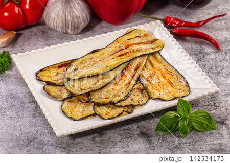 Grilled eggplant slices on white plate with basil and red peppers 142534173