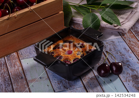 Baked cherry clafoutis in black ceramic dish with fresh cherries and green leaves on rustic wooden table Baked cherry clafoutis in black ceramic dish with fresh cherries and green leaves on rustic wooden table 142534248