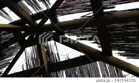 Geometric structure of supporting beams inside a wooden cabin with a reed roof under construction 142534378