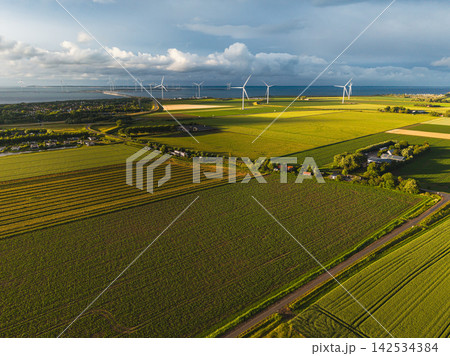 High angle wide horizontal aerial drone photograph of polder fields, farmsteads, wind turbines, storm barrier, and sea in Neeltje Jans, Zeeland, Netherlands in golden hour summer light 142534384