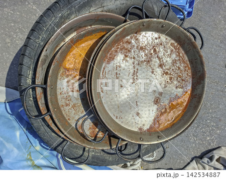 Stacked rusty traditional Spanish paella pans resting on a car tire outdoors in a sunny location Stacked rusty traditional Spanish paella pans resting on a car tire outdoors in a sunny location 142534887