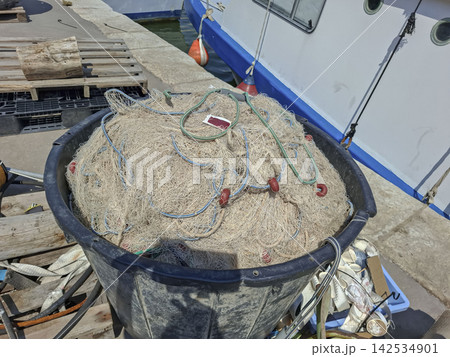 Round black tub filled with fishing netting on dock beside boat hull Round black tub filled with fishing netting on dock beside boat hull 142534901