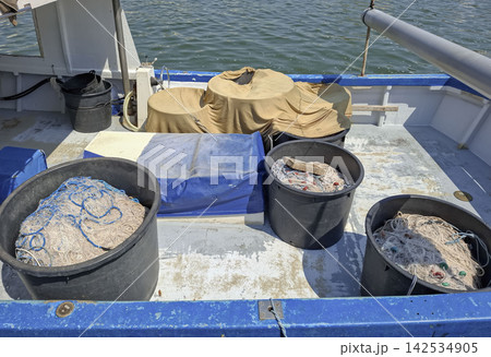 Fishing boat deck with black tubs of fishing nets and gear along blue gunwale 142534905