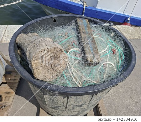 Close up of a tub on a wooden pallet filled with net meshes ropes floats and wooden pieces at a dock 142534910
