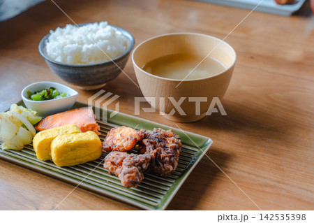 焼き鮭、卵焼き、唐揚げなどが並べられた和定食とご飯・味噌汁のテーブル写真。 焼き鮭、卵焼き、唐揚げなどが並べられた和定食とご飯・味噌汁のテーブル写真。 142535398