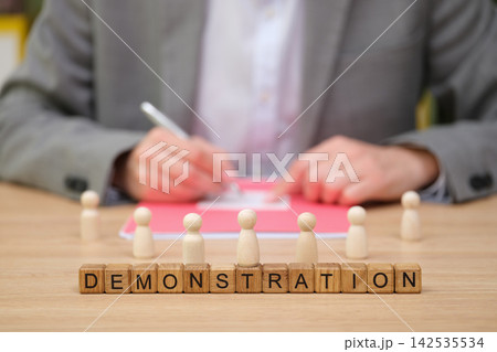 Engaging demonstration with wooden figures and a focused presenter at a table Engaging demonstration with wooden figures and a focused presenter at a table 142535534