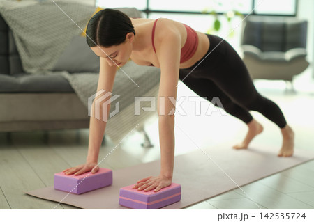 Woman performs plank on straight arms using pink foam yoga blocks 142535724