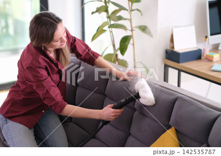 Woman steam cleans sofa backrest during home maintenance Woman steam cleans sofa backrest during home maintenance 142535787