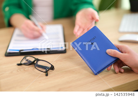 Female tourist gives passport to travel agent at desk in office Female tourist gives passport to travel agent at desk in office 142535948