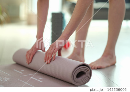 Fit woman rolls yoga mat after finishing home workout session Fit woman rolls yoga mat after finishing home workout session 142536003