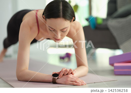 Focused woman stands in plank pose and checks heartbeat rate 142536258