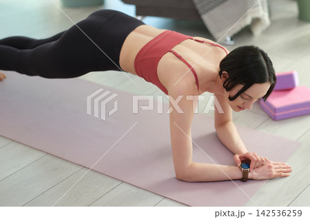 Young woman controls health data with fitness tracker in plank Young woman controls health data with fitness tracker in plank 142536259