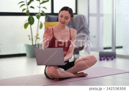 Friendly sportswoman conducts broadcast via laptop at home 142536308