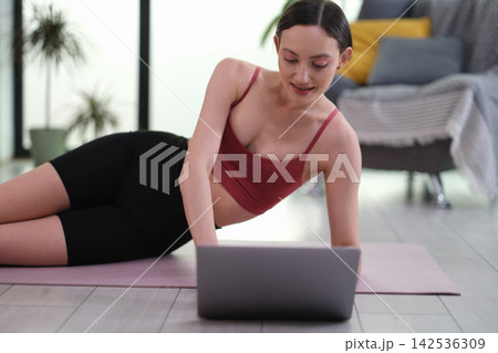 Smiling woman athlete watches video lesson via laptop at home 142536309