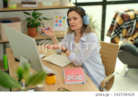 Businesswoman speaks during online meeting with headphones Businesswoman speaks during online meeting with headphones 142536428