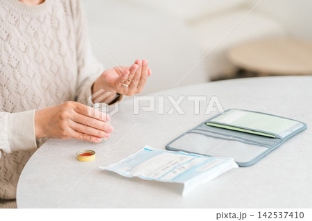 家で処方薬を手に取るシニア女性の手元。毎日の服薬と薬の管理 家で処方薬を手に取るシニア女性の手元。毎日の服薬と薬の管理 142537410