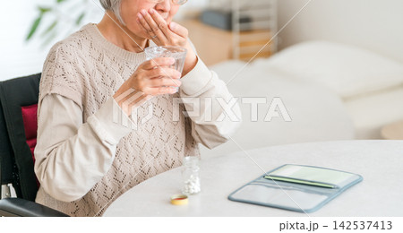 自宅で薬を水と一緒に服用するシニア女性。日常の服薬と健康管理 142537413