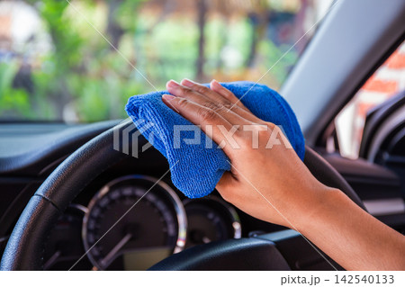 Hand with microfiber cloth cleaning Interior and steering wheel modern car. 142540133