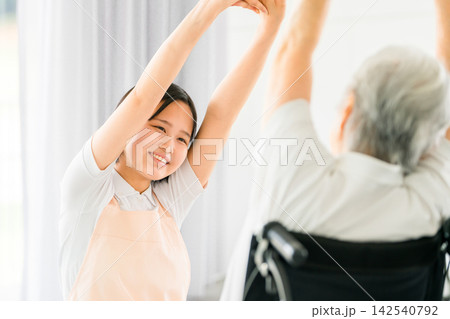 車椅子のシニア女性と一緒にストレッチをする笑顔の介護スタッフ 車椅子のシニア女性と一緒にストレッチをする笑顔の介護スタッフ 142540792