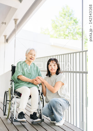 車椅子で過ごすシニア女性に寄り添い手を握る娘との笑顔の親子 車椅子で過ごすシニア女性に寄り添い手を握る娘との笑顔の親子 142543168