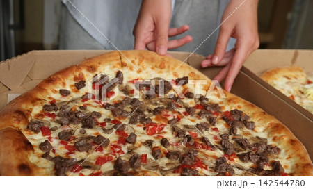 Meat pizza with mushrooms and tomatoes being taken out of a cardboard box Meat pizza with mushrooms and tomatoes being taken out of a cardboard box 142544780