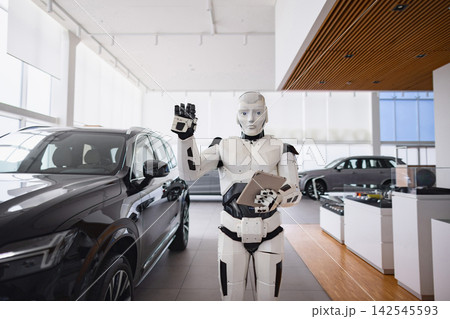 A humanoid robot stands in a modern car dealership, holding a tablet and gesturing with its hand 142545593