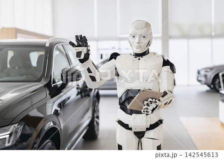 A humanoid robot stands in a car dealership, holding a tablet and waving, ready to assist customers with vehicle purchases A humanoid robot stands in a car dealership, holding a tablet and waving, ready to assist customers with vehicle purchases 142545613