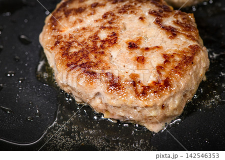 鉄板で焼くハンバーグ、ジューシーな肉汁とこんがりした焼き目が食欲をそそる調理シーン 142546353