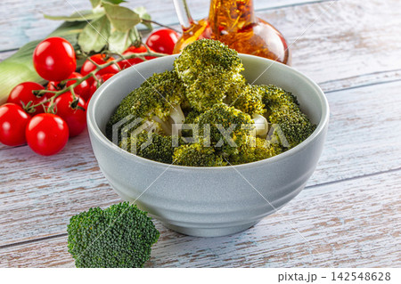 Steamed broccoli florets in gray bowl with cherry tomatoes and olive oil on rustic wood 142548628