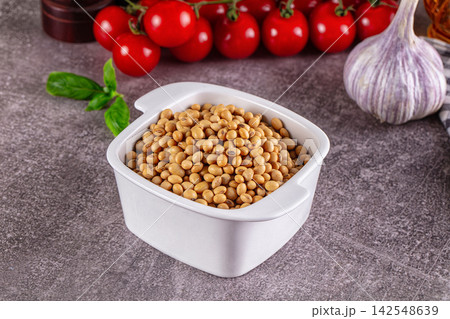 Soybeans in white ceramic bowl with cherry tomatoes and garlic on textured surface 142548639