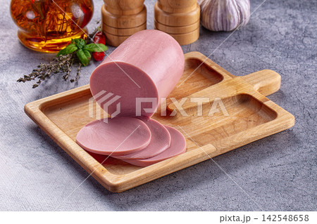 Sliced pink deli meat on wooden cutting board with herbs and garlic 142548658