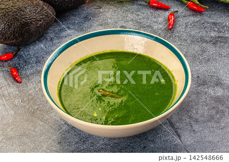 Green spinach cream soup in ceramic bowl with avocado and red chili peppers on gray stone background Green spinach cream soup in ceramic bowl with avocado and red chili peppers on gray stone background 142548666