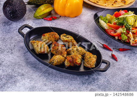 Minced chicken kebab pieces in black dish with fresh salad and vegetables background Minced chicken kebab pieces in black dish with fresh salad and vegetables background 142548686