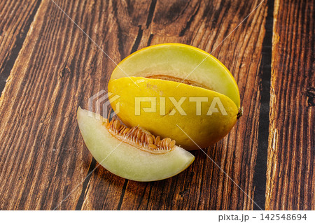 Halved yellow melon with slice on rustic wooden surface Halved yellow melon with slice on rustic wooden surface 142548694