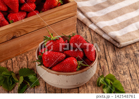 Fresh red strawberries in ceramic bowl on rustic wooden table with green leaves and striped cloth Fresh red strawberries in ceramic bowl on rustic wooden table with green leaves and striped cloth 142548761