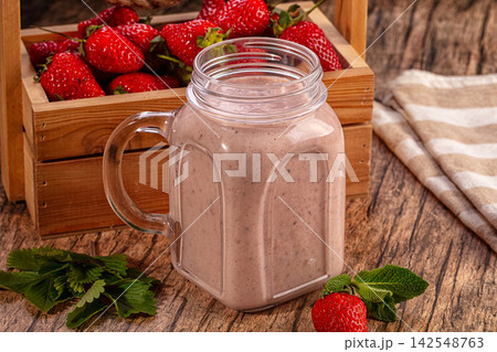 Strawberry milkshake in glass jar with fresh strawberries and mint on rustic wood 142548763
