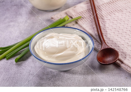 Creamy yogurt in ceramic bowl with green onions and wooden spoon on textured surface 142548766