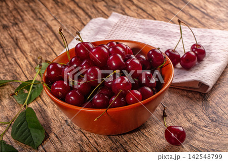 Fresh ripe cherries in rustic ceramic bowl on wooden table with green leaves Fresh ripe cherries in rustic ceramic bowl on wooden table with green leaves 142548799